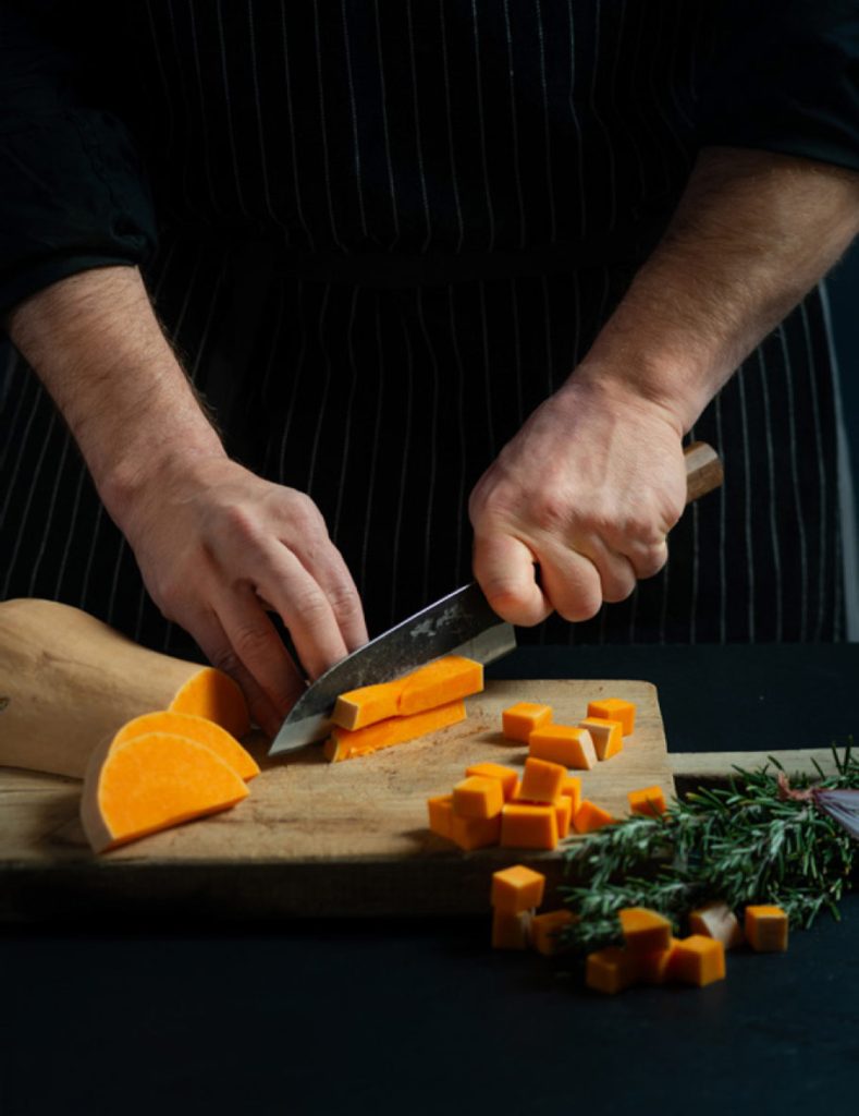 Chef intento a tagliare una zucca su un tagliere, con ingredienti freschi in vista