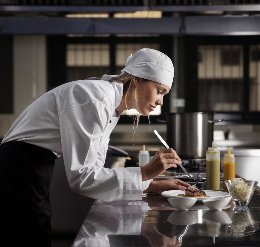 Una chef donna mentre cucina e prepara ingredienti in una cucina professionale.